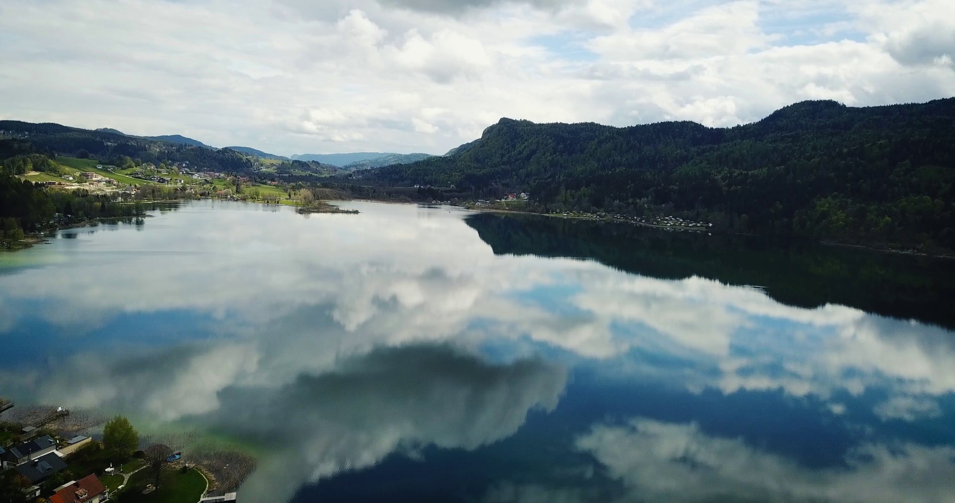 Wolken spiegeln sich im ruhigen See, eingerahmt von bewaldeten Hügeln